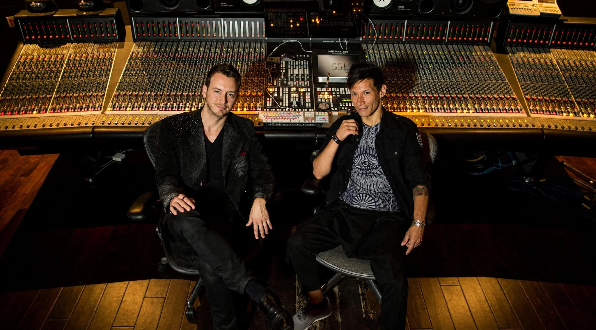 Reuel and Jordan Kolar sitting in front of a large sound mixing console in a recording studio.