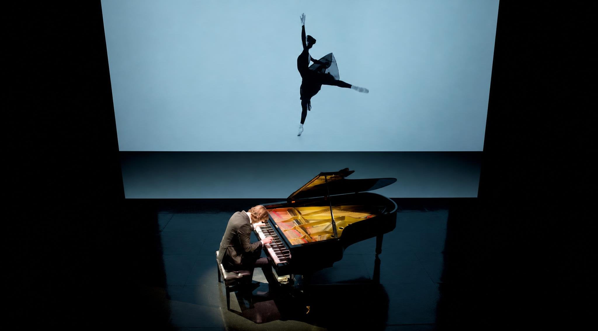 Reuel playing a grand piano on stage with a large image of a ballet dancer projected behind him.