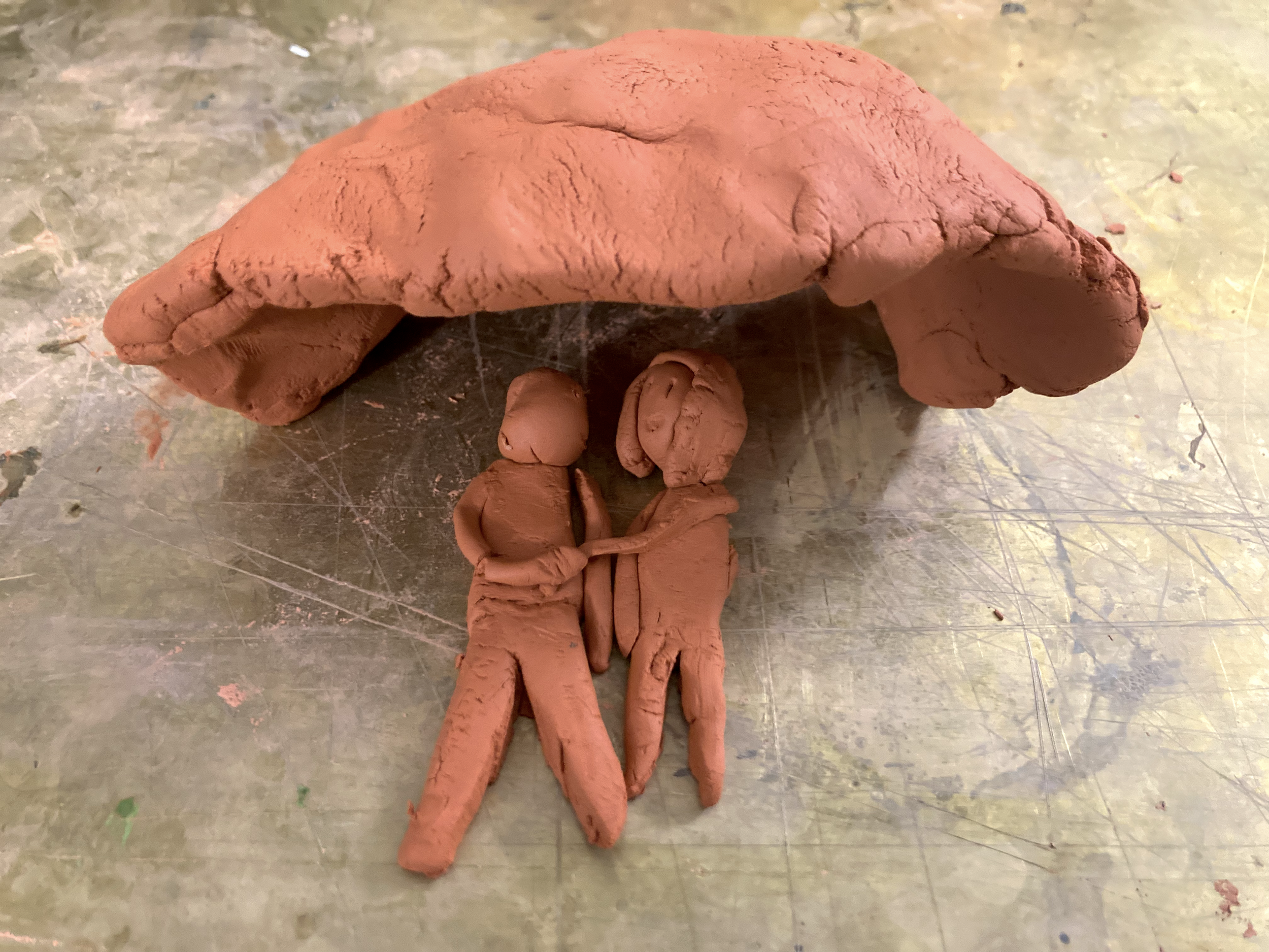 Sculptură din lut a două personaje care se țin de mână sub o arcadă mare, curbată.