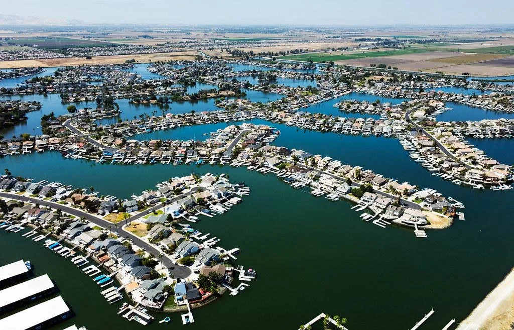 Aerial view of a residential marina with houses and boats on a waterway, surrounded by farmland and open fields in the distance.