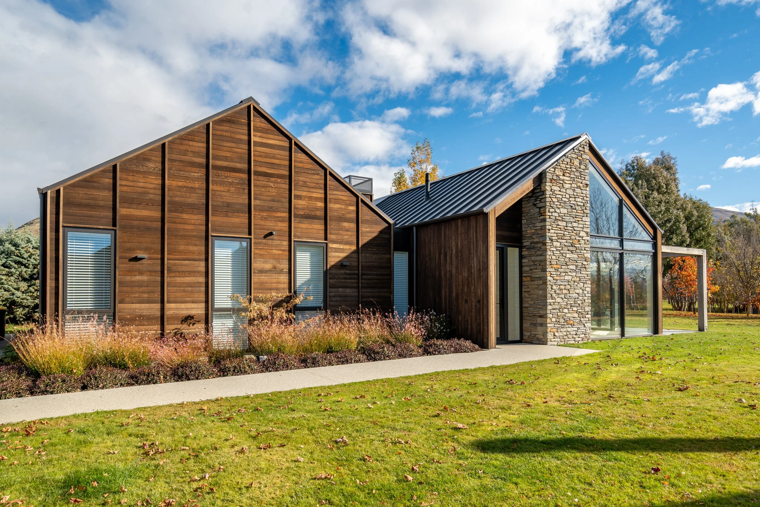 Dark cedar and schist-clad Alpine Residence with dramatic gable forms and landscaped grounds in Wānaka.