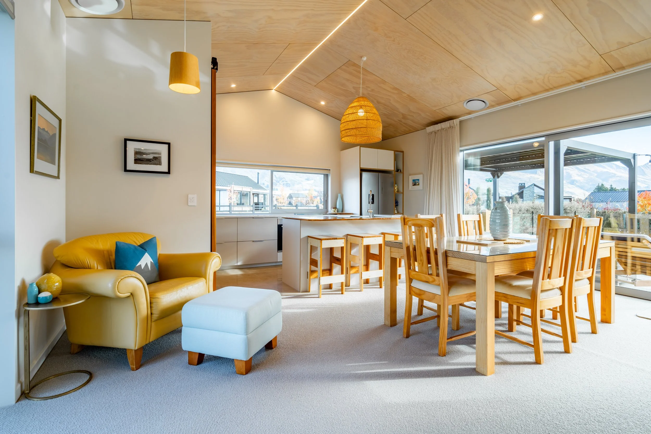 Open-plan kitchen and dining space with vaulted plywood ceiling and large sliding doors to outdoor living.