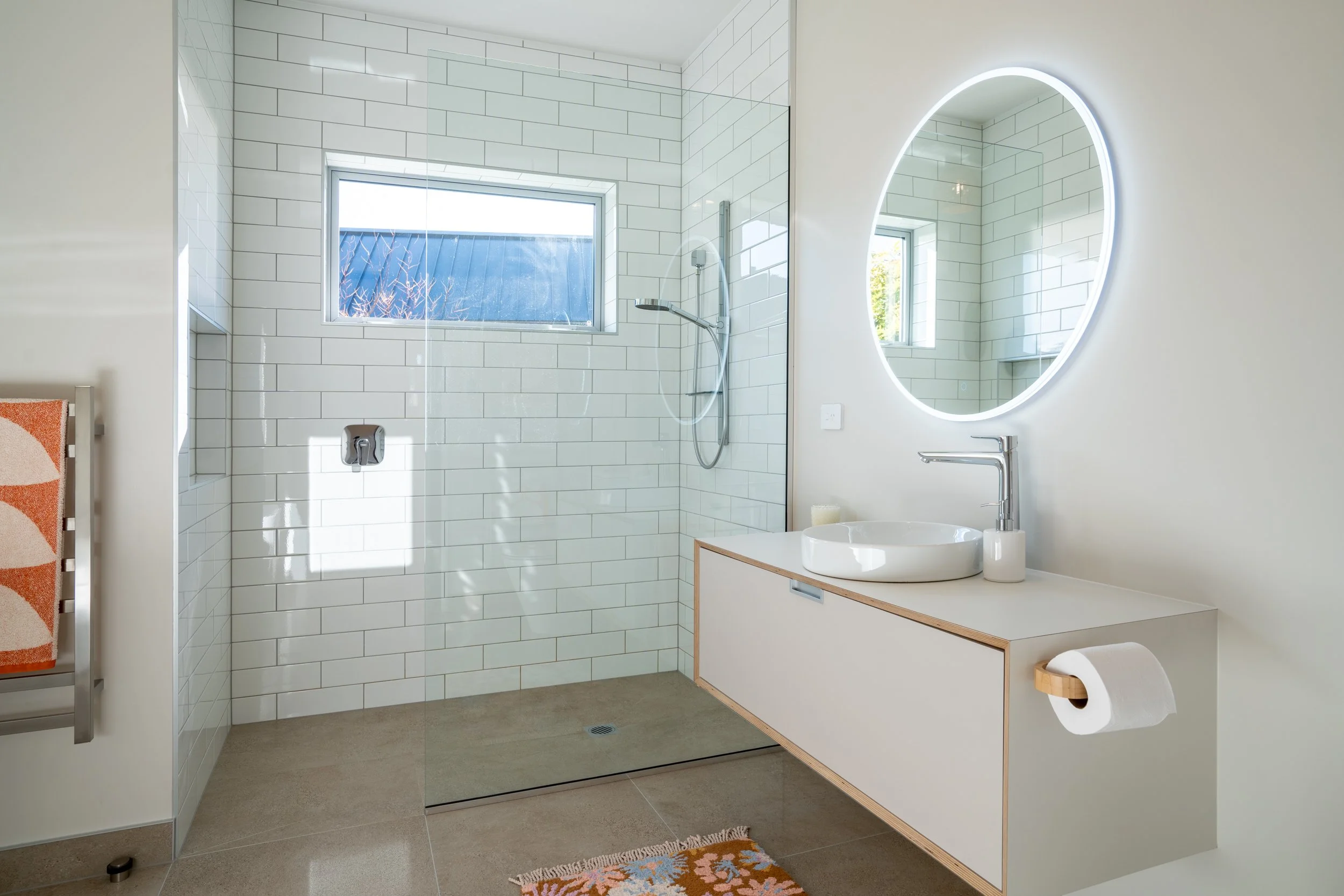 Minimalist bathroom with tiled walk-in shower, floating vanity and soft natural light.