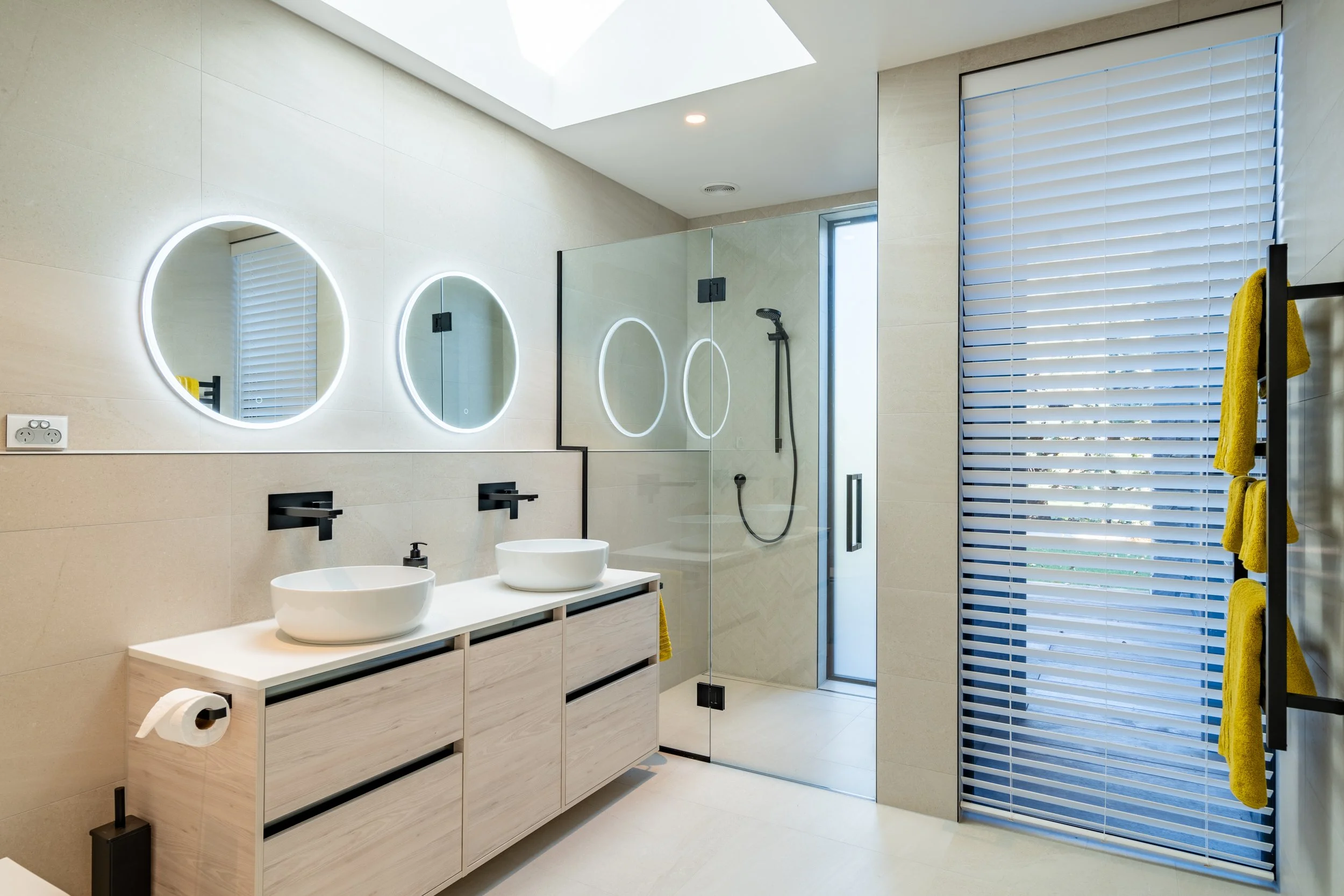 Minimalist ensuite bathroom with double vanity, circular mirrors and walk-in tiled shower.