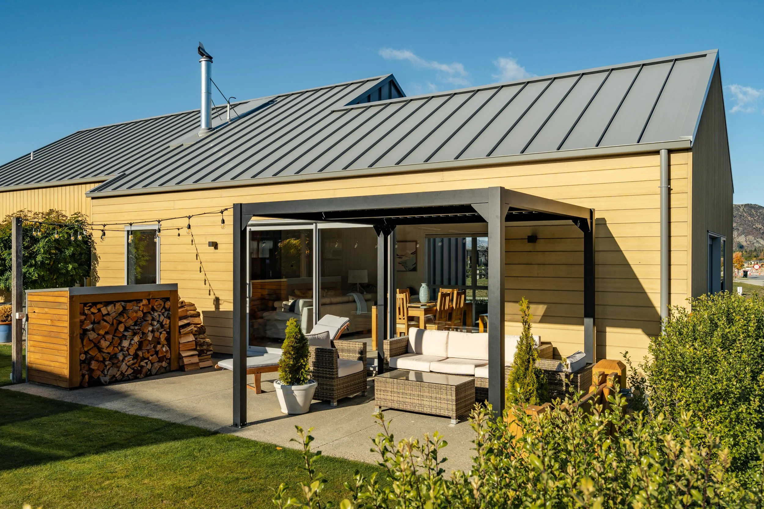 Outdoor living area with covered pergola and cedar cladding at Marjon Residence in Wānaka.