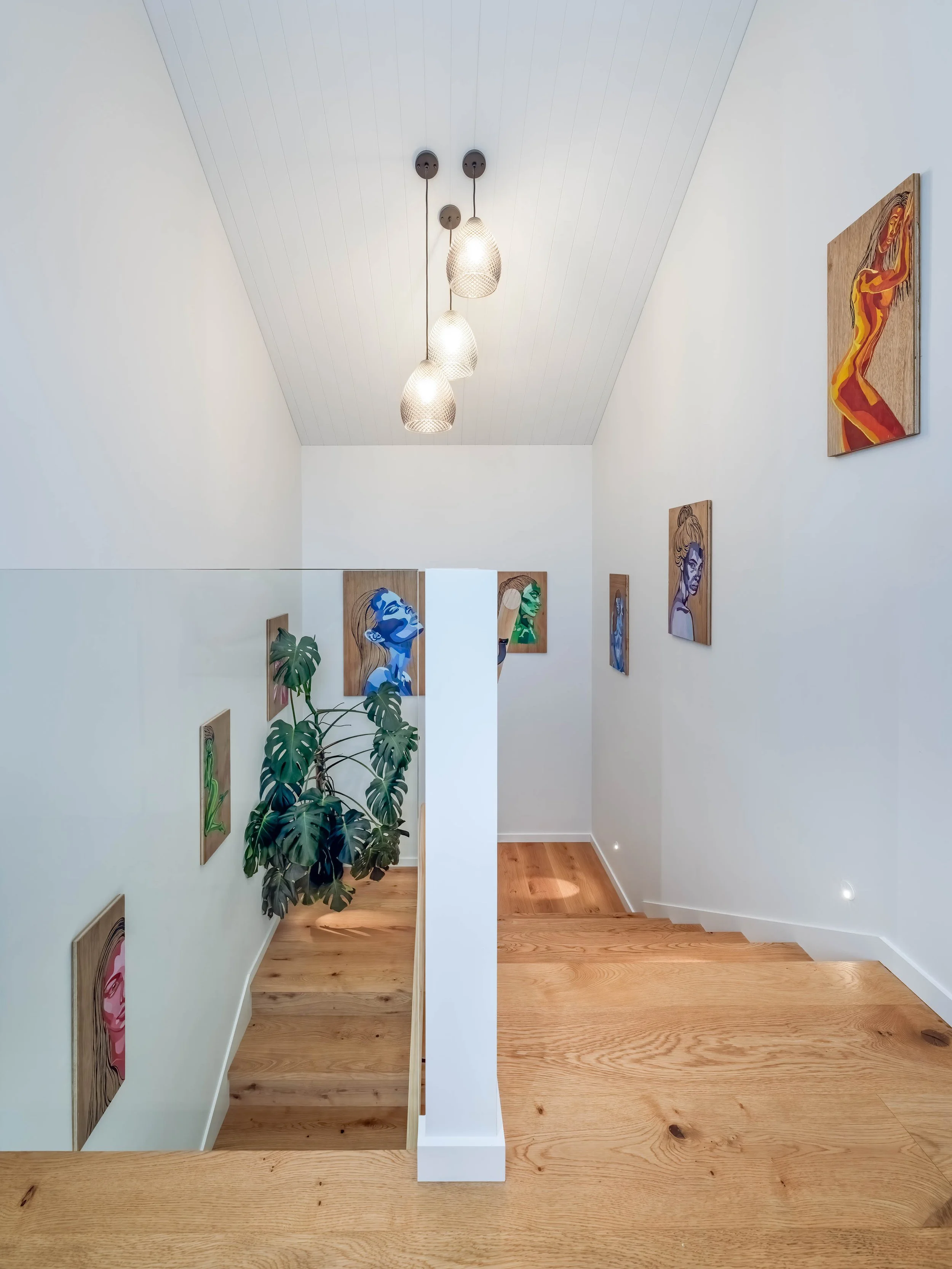 Stairway featuring warm timber flooring, a glass balustrade, and feature pendant lights. 