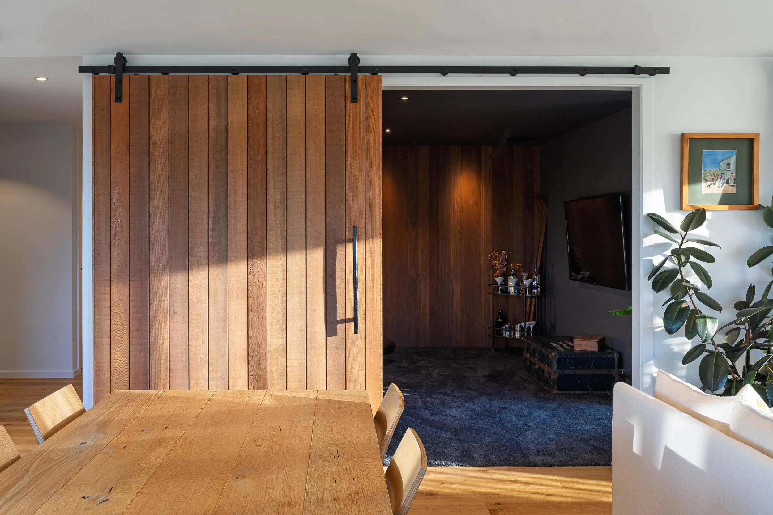 A timber sliding barn door reveals a cosy, plushly-carpeted movie den off of the main lounge space. 