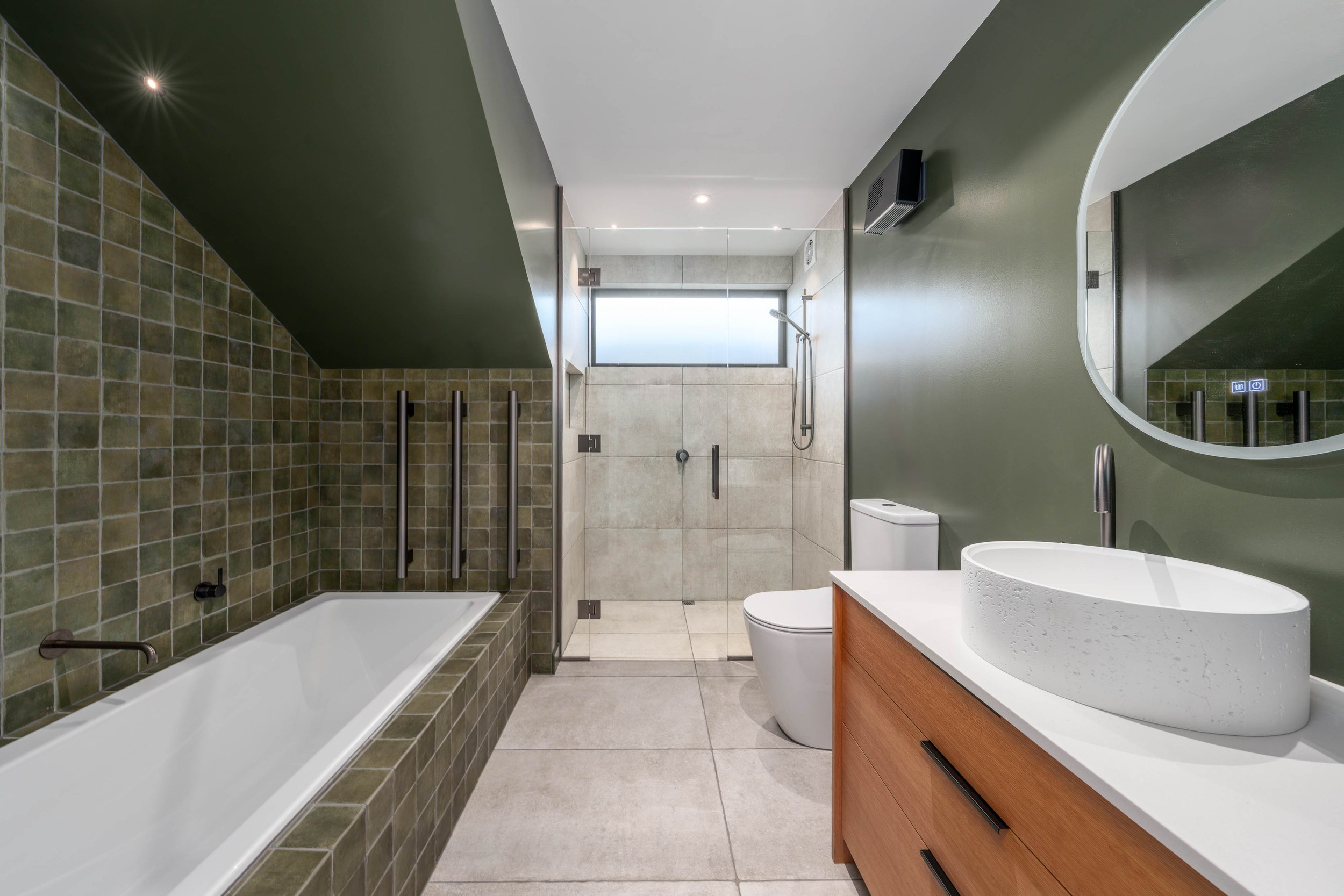 Earthy family bathroom featuring a bathtub, textured tile feature wall, and natural light. 