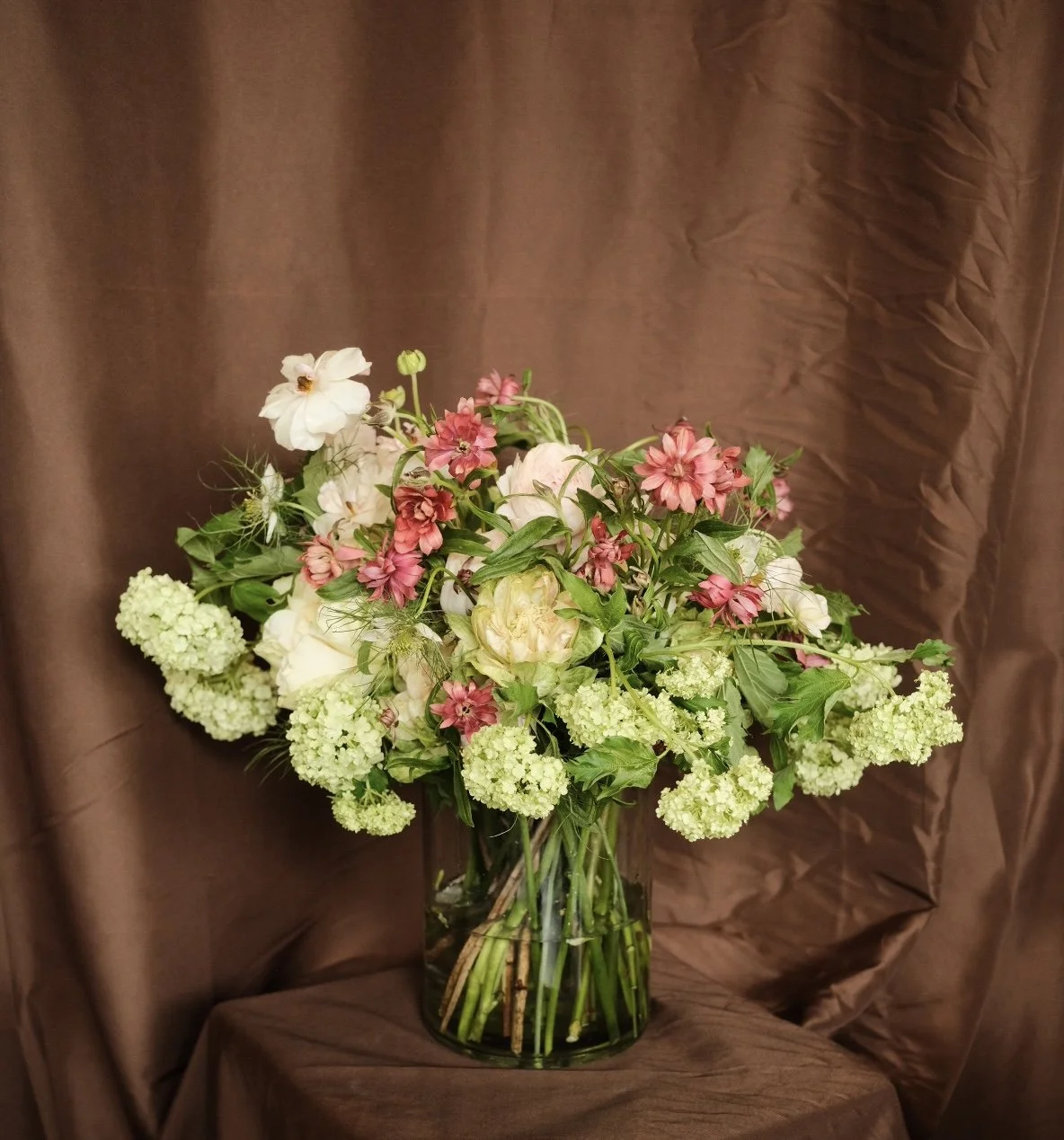 Ramo de flores en un jarrón con fondo de tela marrón.