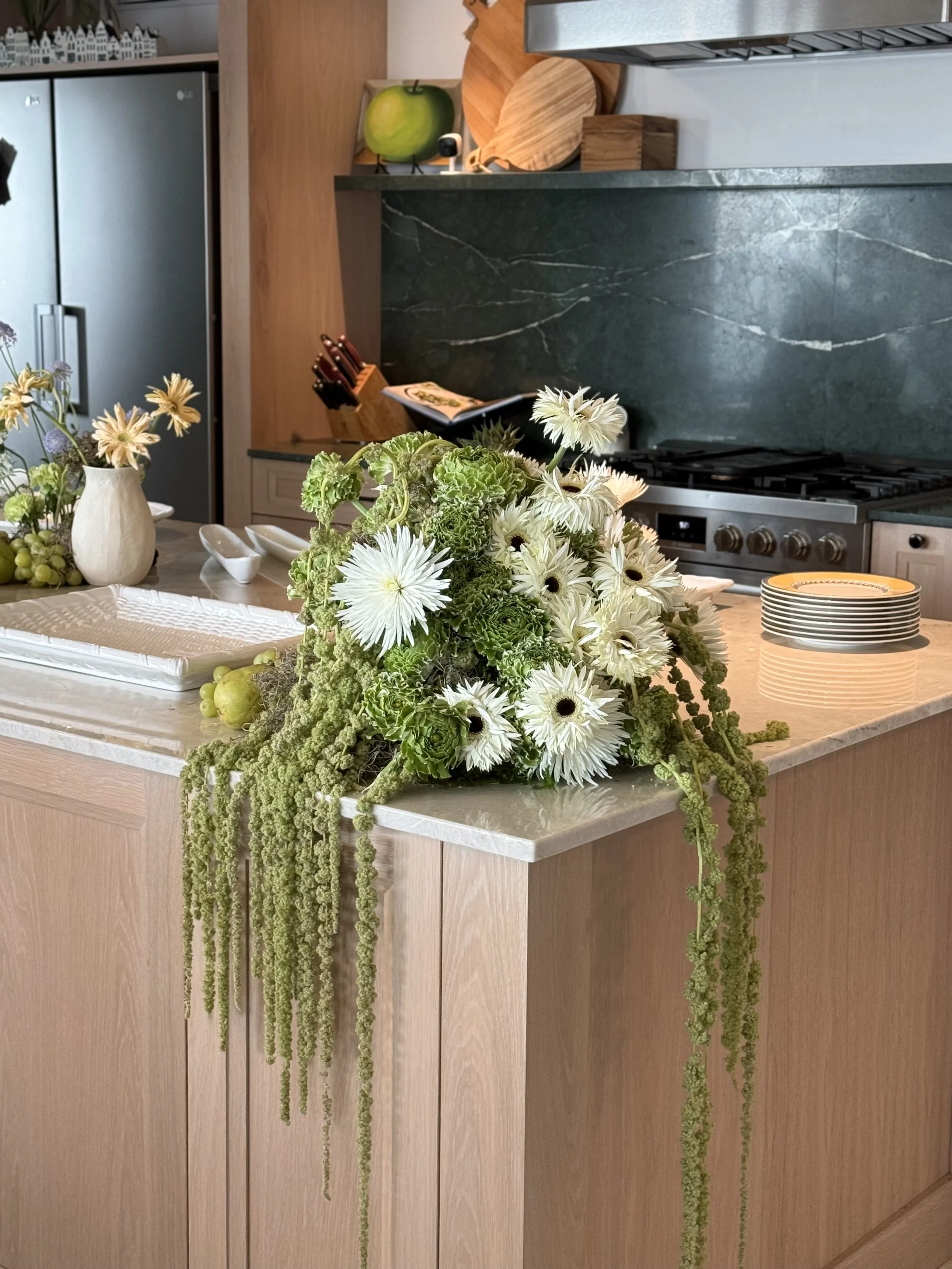 Un arreglo de flores blancas y verdes en una mesa de madera en una cocina moderna con electrodomésticos de acero inoxidable y utensilios de cocina de madera.
