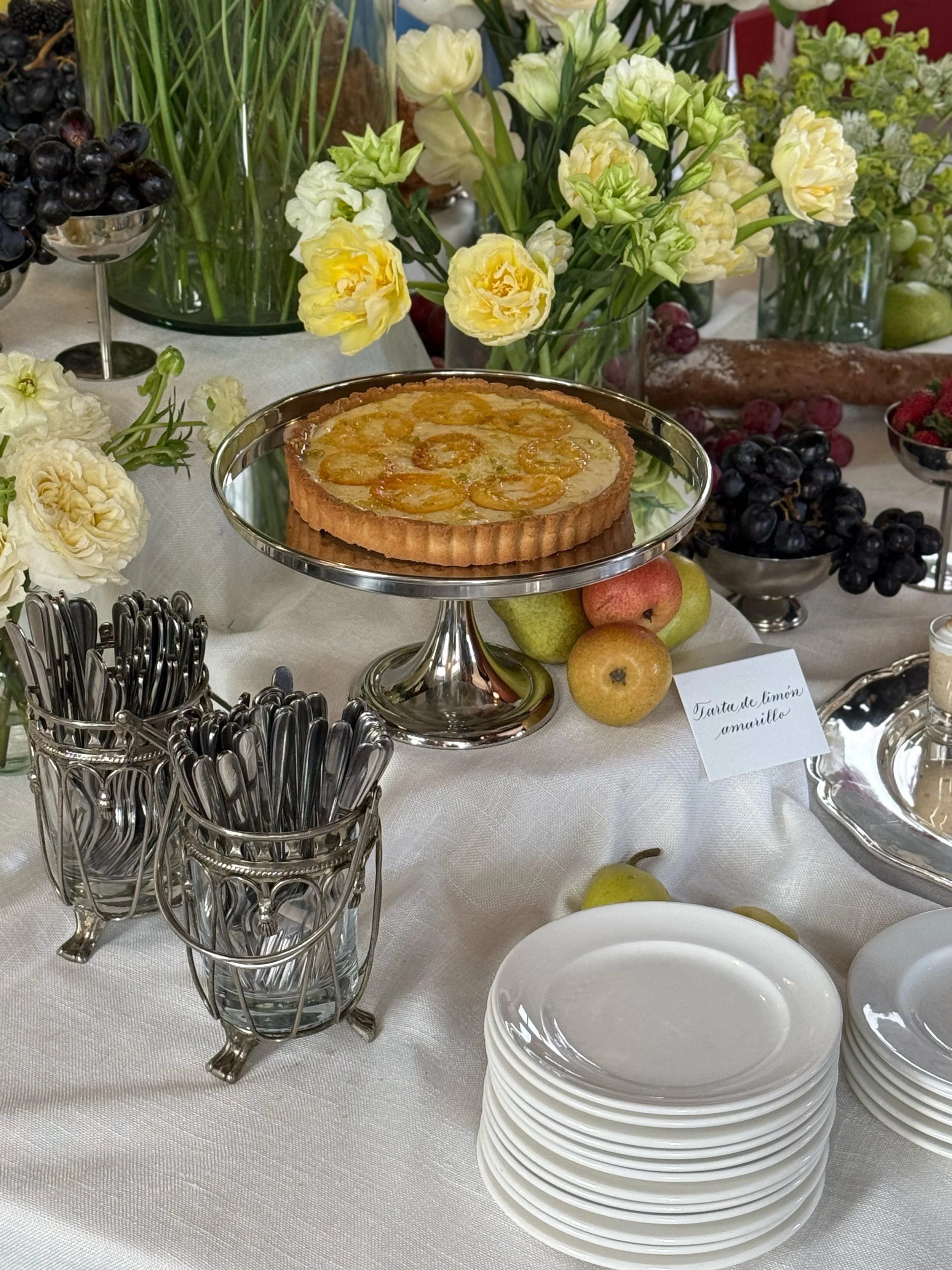 Tarta de limón amarillo en plato plateado en mesa con flores y fruta