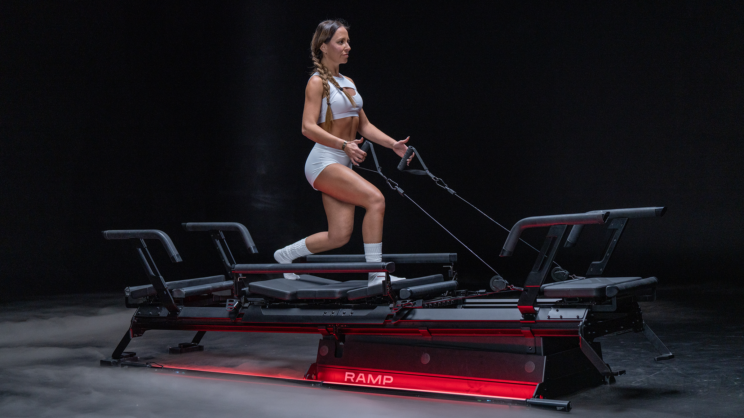 A woman in athletic clothing is using a futuristic exercise machine with a dark background.