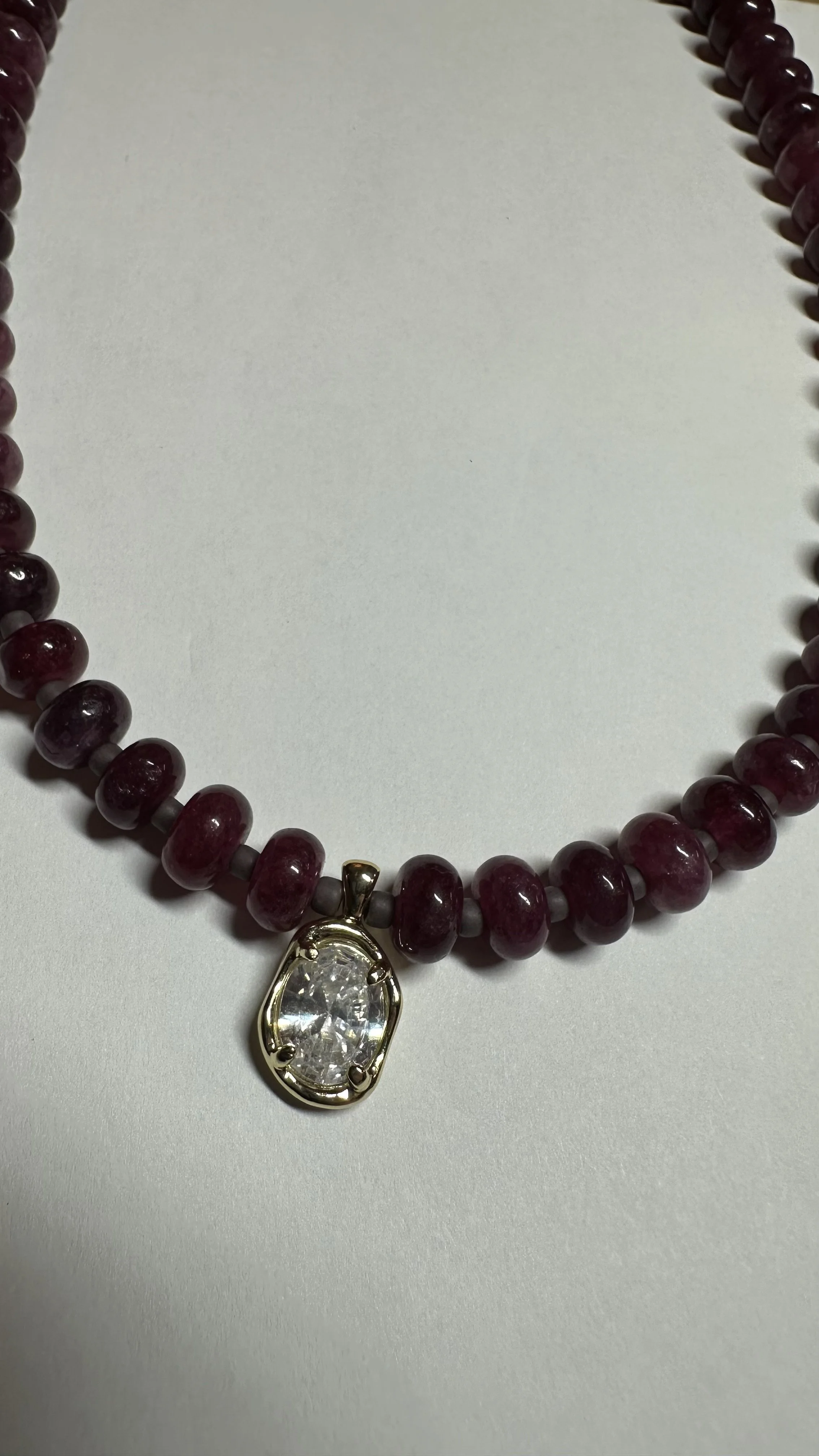 Necklace with purple beads and a large clear gemstone pendant on a white background.