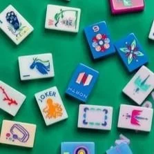 Collection of colorful domino tiles with various images and symbols, including a crab, a butterfly, a French flag, and playing card suits, scattered on a green surface.