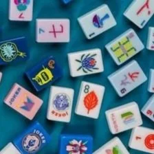Collection of colorful printed Mahjong tiles featuring various numbers, symbols, and images, scattered on a blue surface.