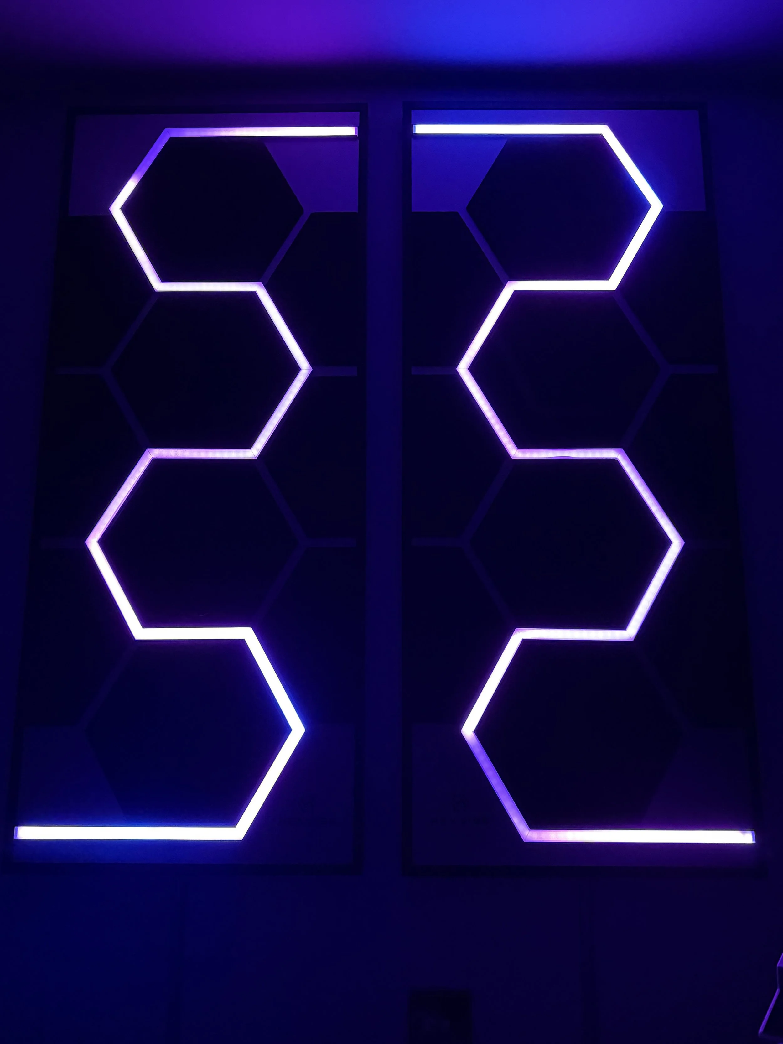 Two illuminated HexVIBE FLOW acoustic panels with geometric sound-reactive LED lighting.