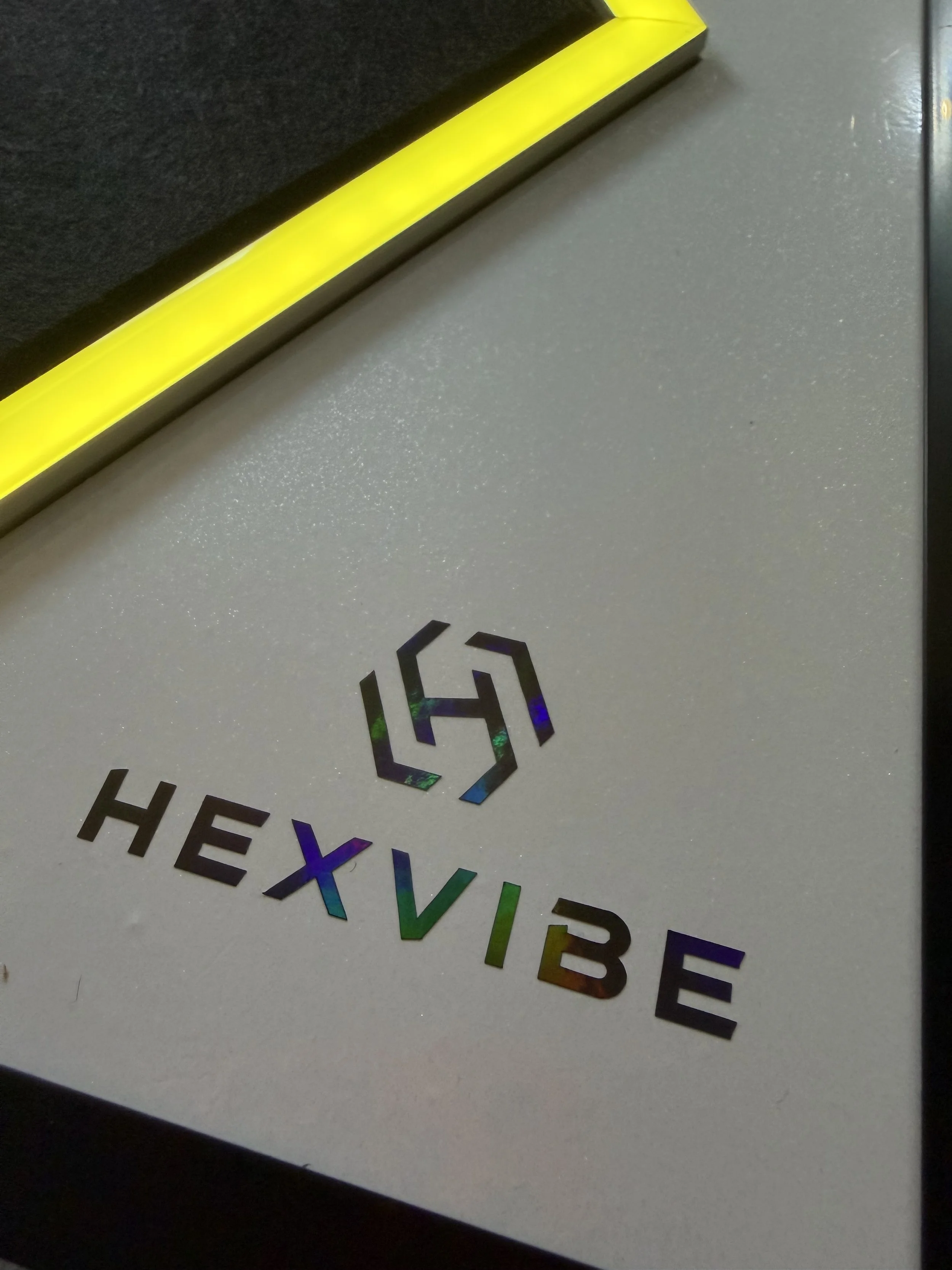 Close-up of a handcrafted HexVIBE Flash sound-reactive LED acoustic panel with illuminated yellow LED channels and premium holographic HexVIBE branding.