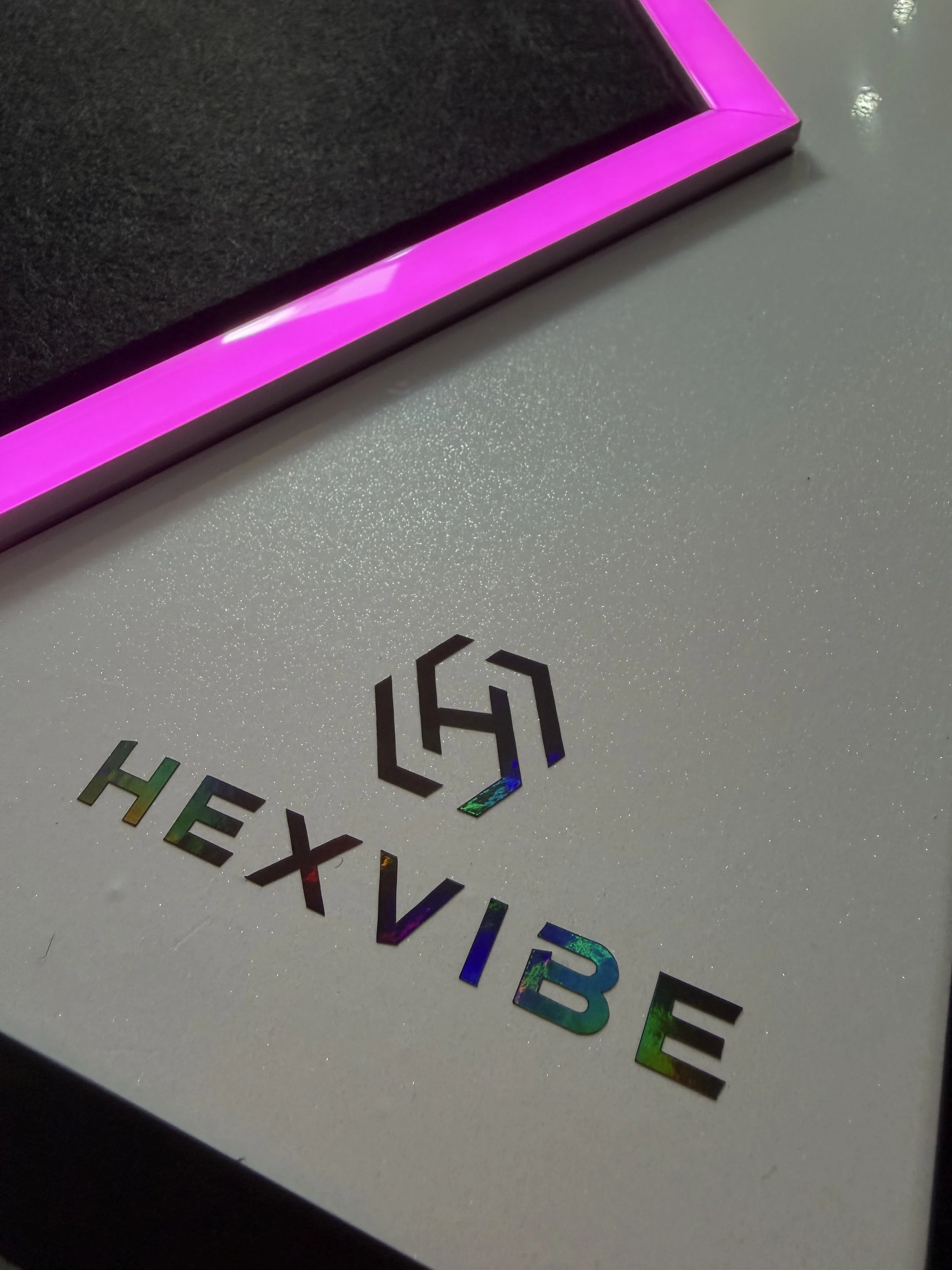 Close-up of a handcrafted HexVIBE Flash sound-reactive LED acoustic panel with illuminated pink LED channels and premium holographic HexVIBE branding.
