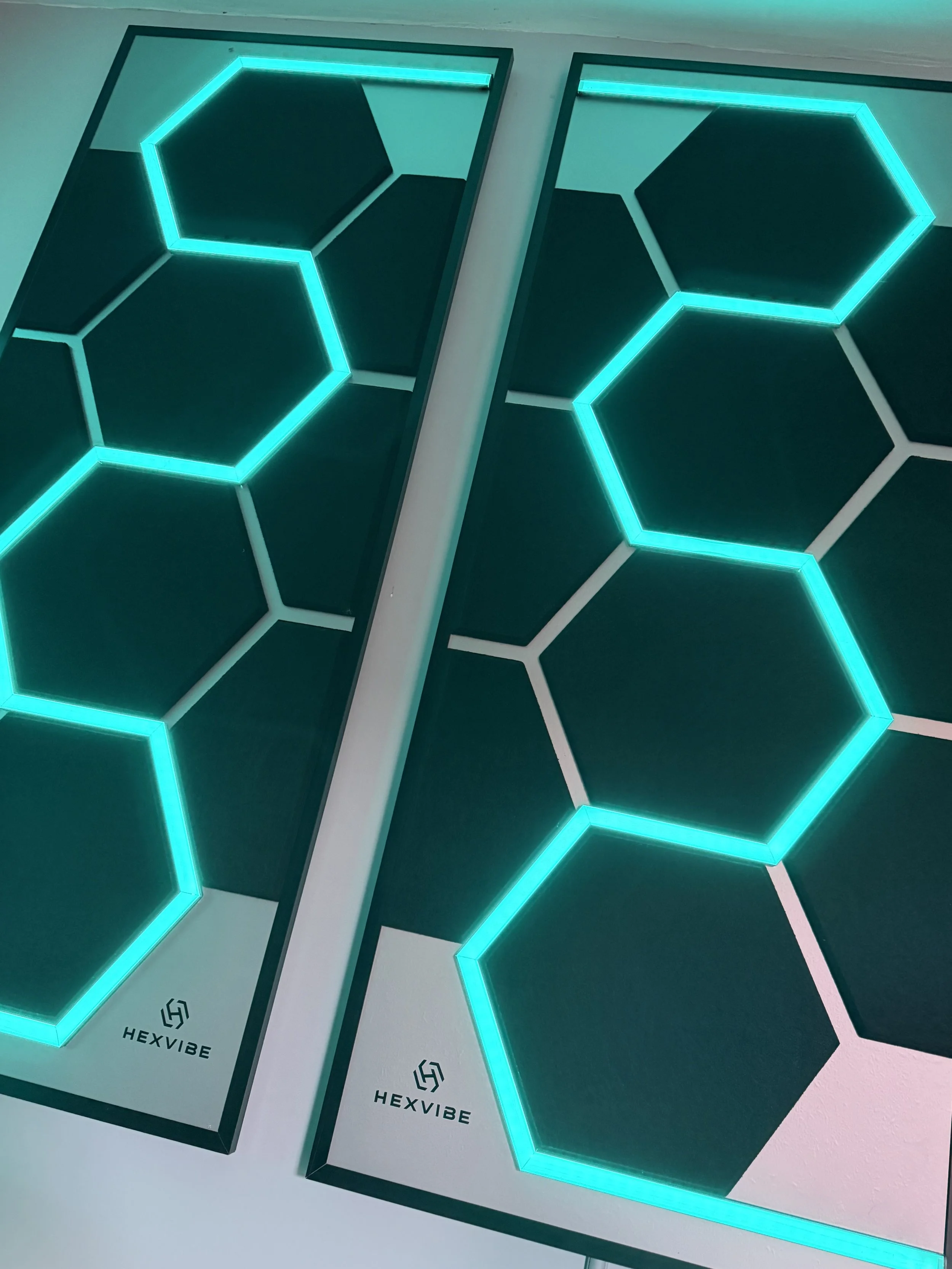Two HexVIBE Flash sound-reactive LED acoustic panels illuminated in blue, showcasing the signature hexagonal lighting design.