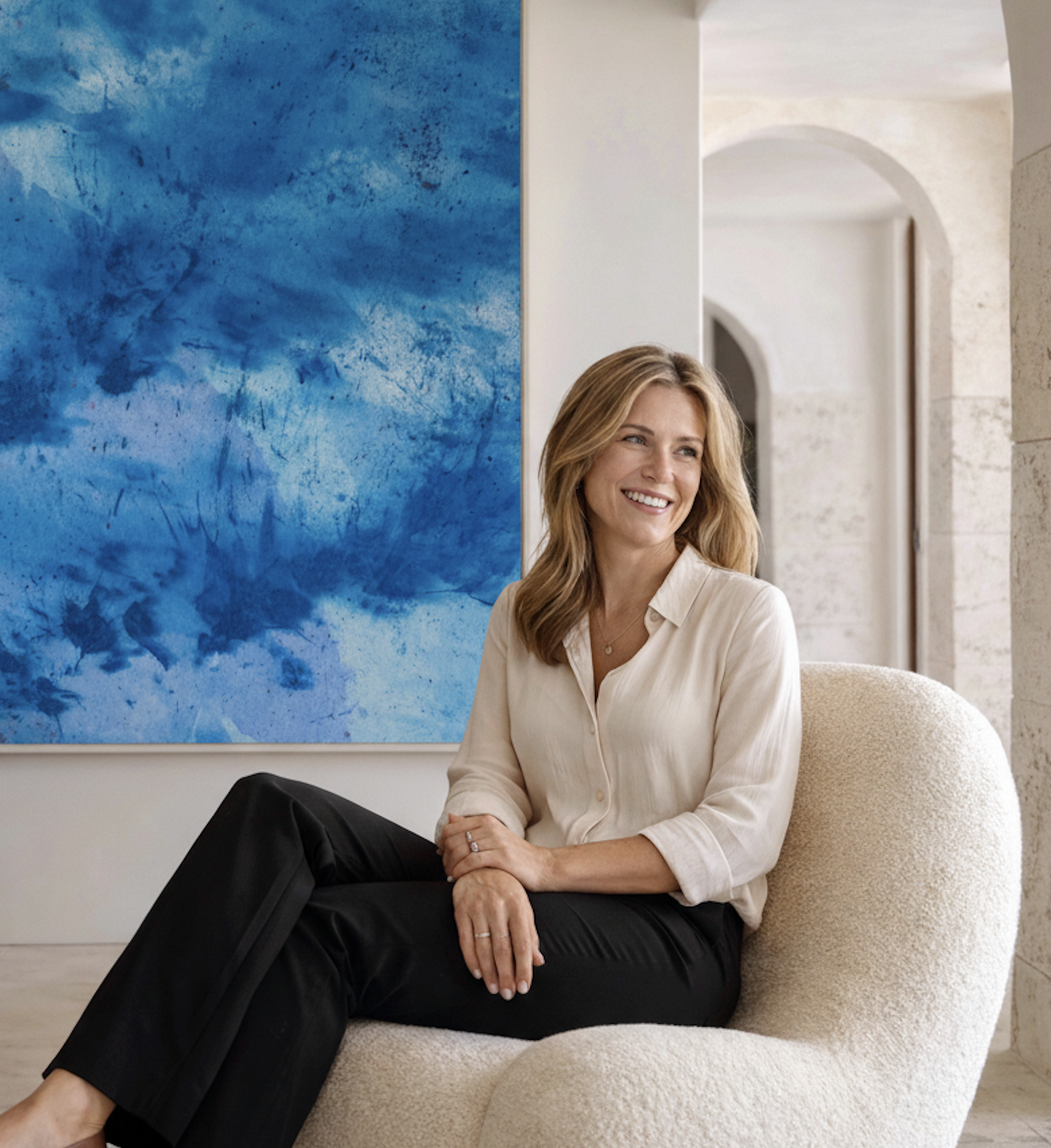 Woman sitting on a beige armchair in an art gallery, smiling, with a large blue abstract painting behind her.
