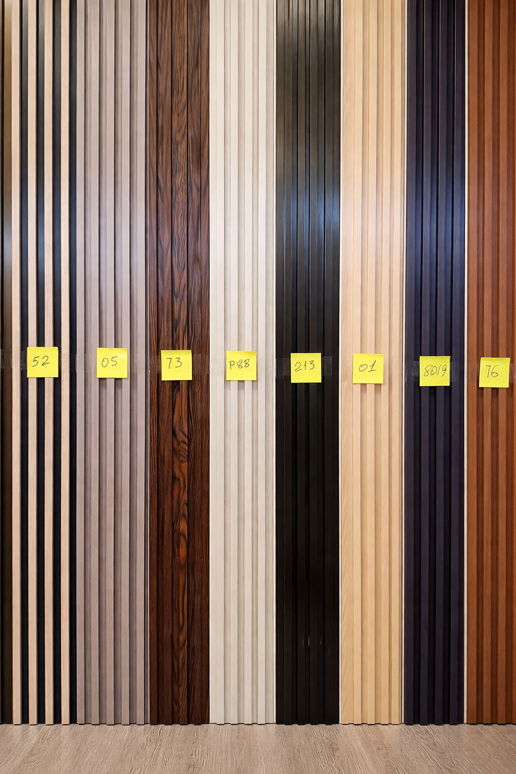 Display of wood and laminate flooring samples arranged in vertical strips with yellow sticky notes labeled with codes.