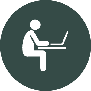 Icon of person sitting at a desk using a laptop.