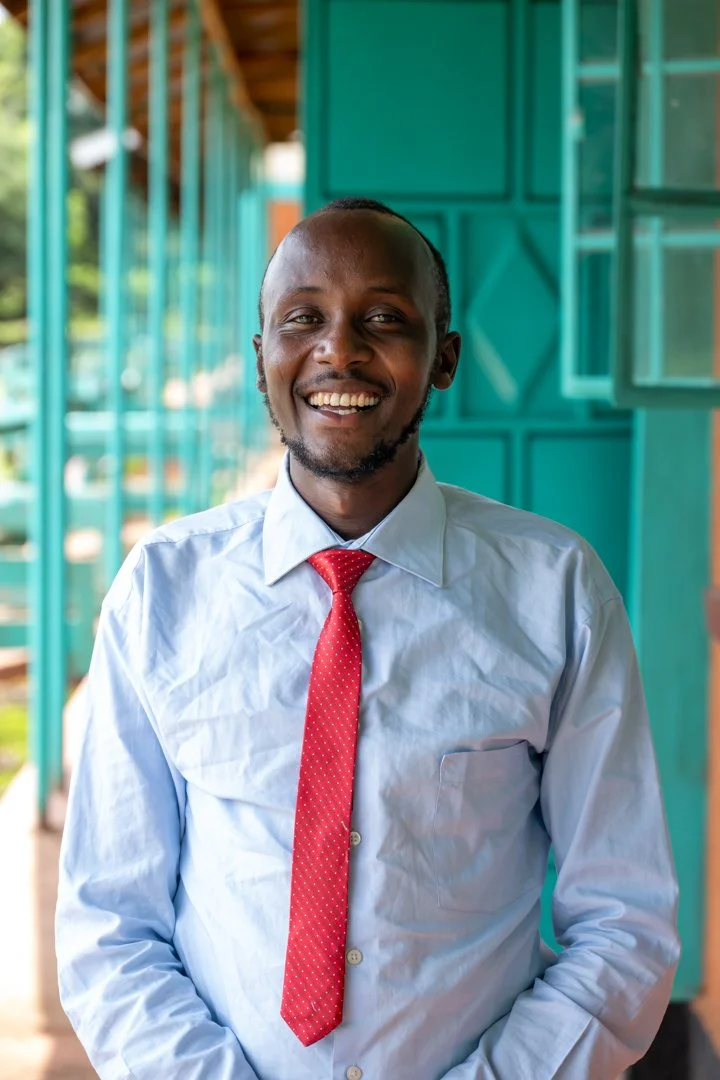 A smiling man in a white shirt and red tie standing outdoors near teal-colored structures.