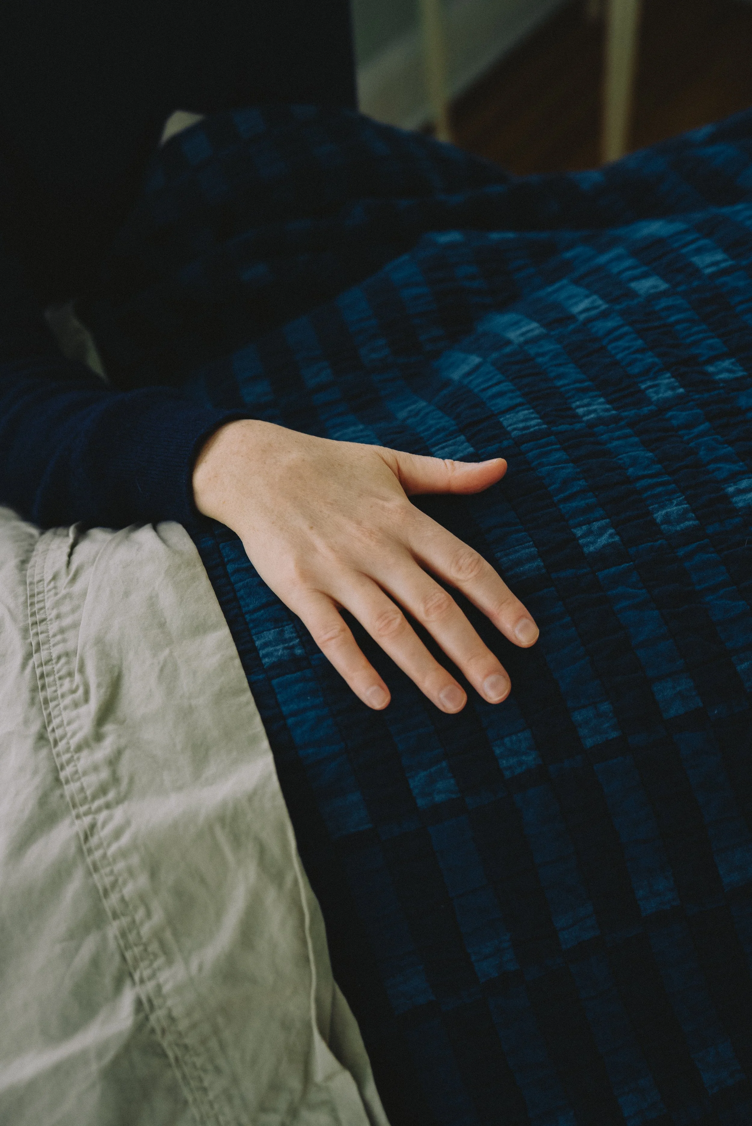 A person's hand resting on a quilted, dark blue blanket with a checkered pattern, beside beige pants.