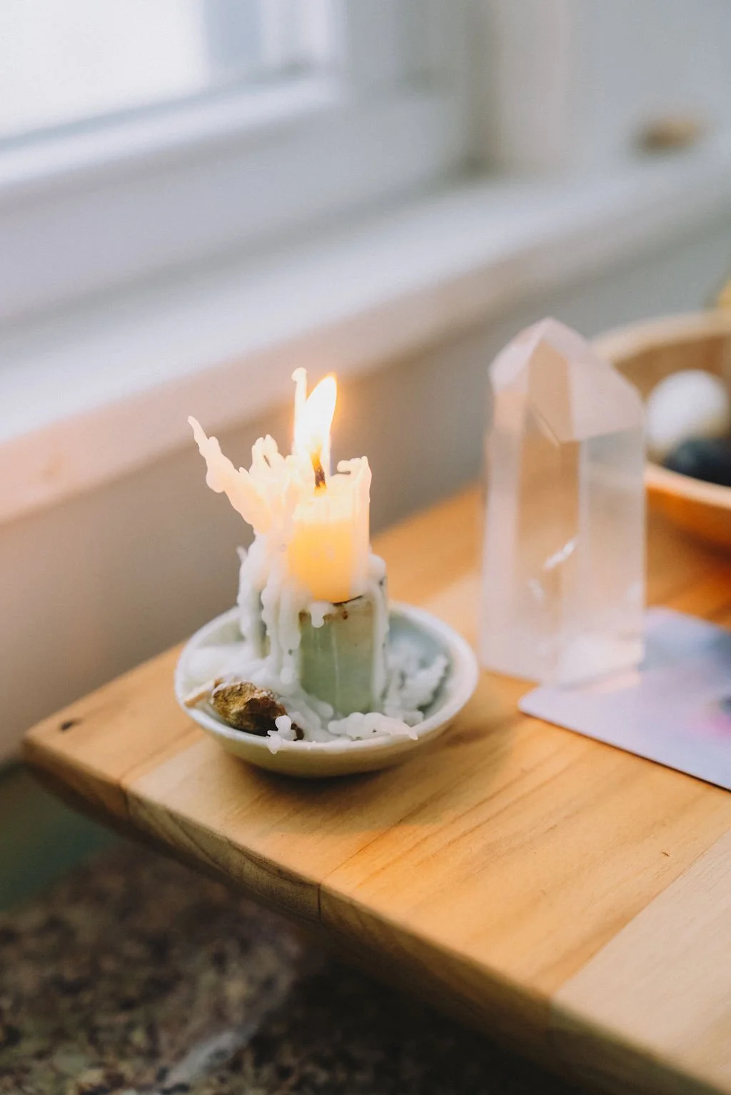A birthday candle that is melting on a small dish with melted wax dripping down, placed on a wooden table