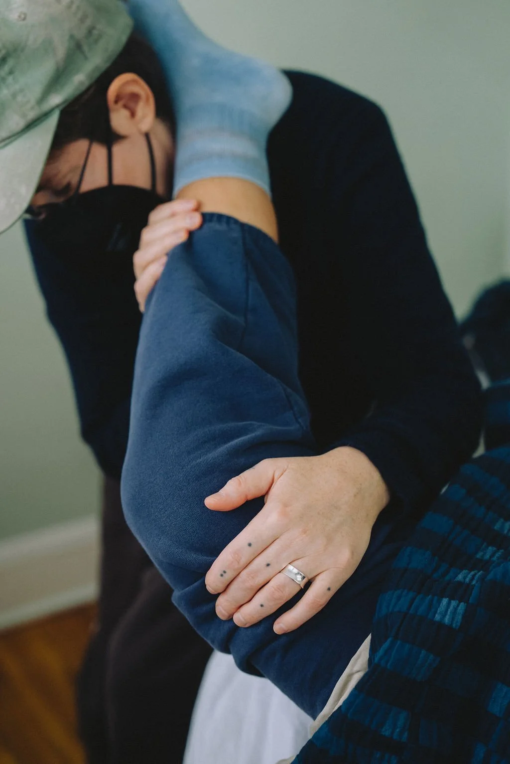 A chiropractor performing a spinal adjustment on a patient lying face down. The chiropractor's hands are on the patient's back, and the patient is wearing a black face mask.