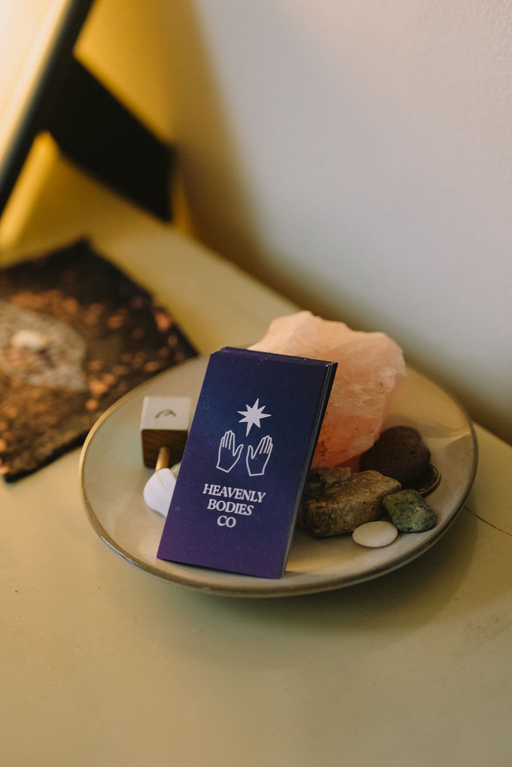 A small decorative display on a table featuring a card with the logo and name of Heavenly Bodies Co, surrounded by various rocks and minerals
