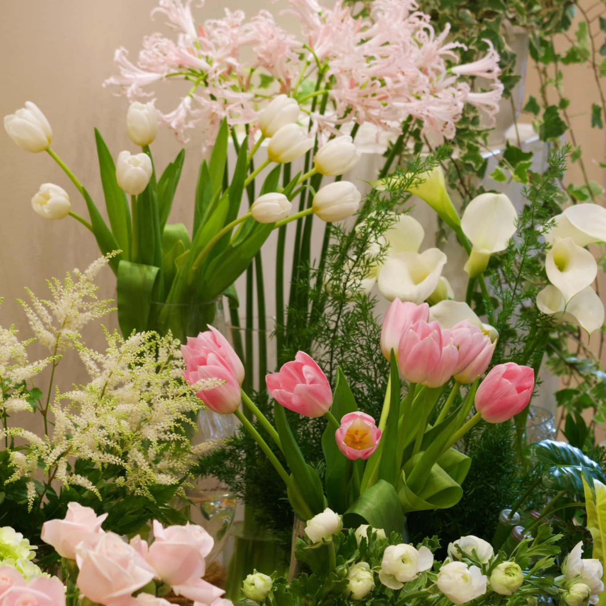 A collection of various fresh flowers including white tulips, pink tulips, white calla lilies, and other small white flowers arranged together.