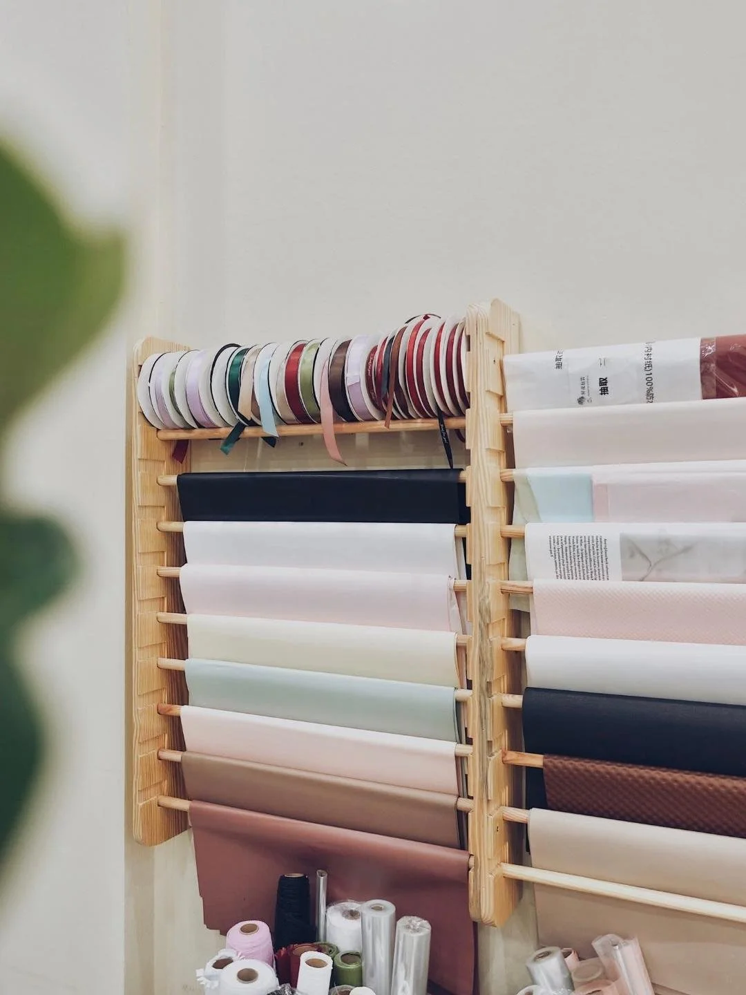 Display of assorted fabric or ribbon rolls arranged on a wooden rack, with spools of thread and other sewing supplies at the bottom.