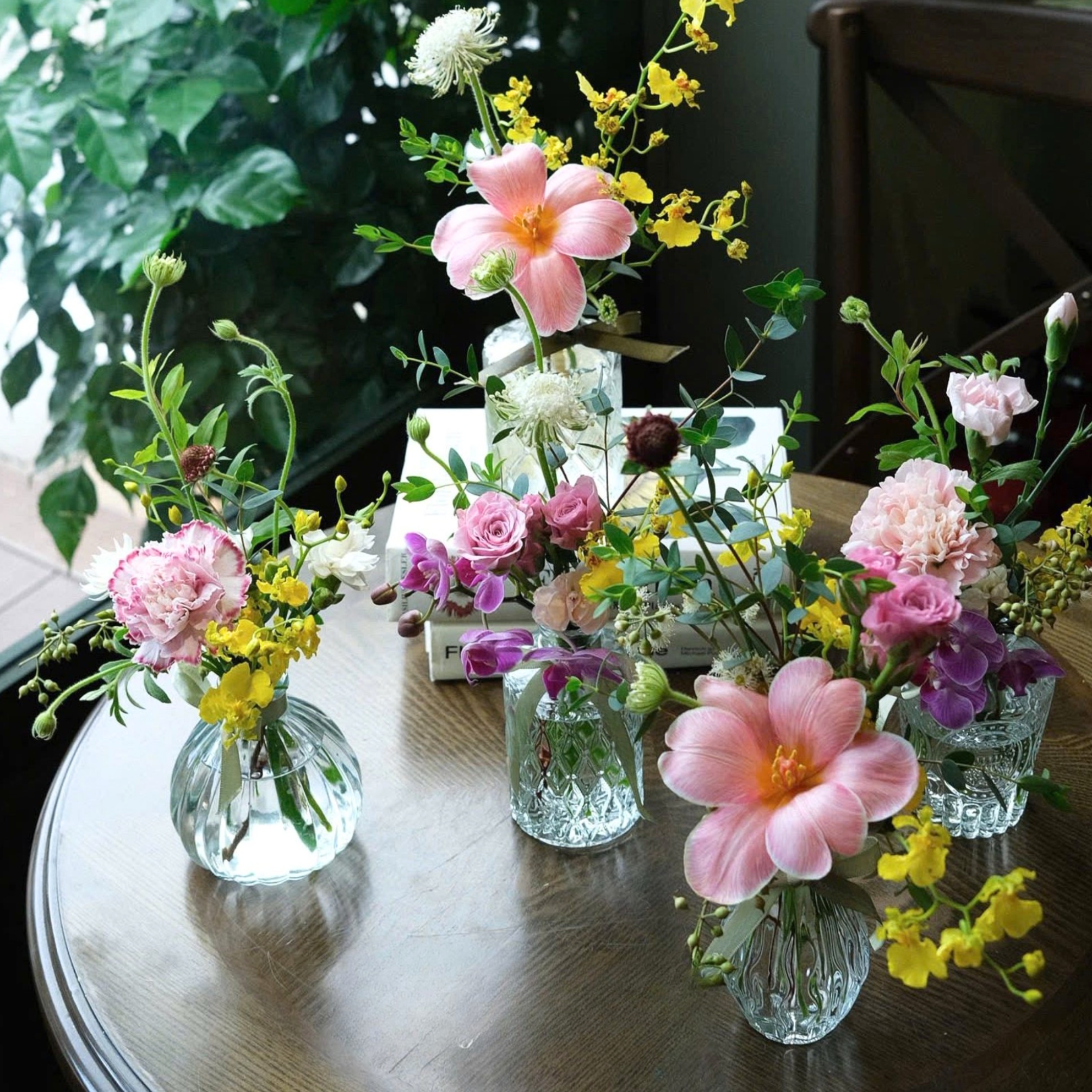 Multiple small vases with various colorful flowers placed on a wooden table.