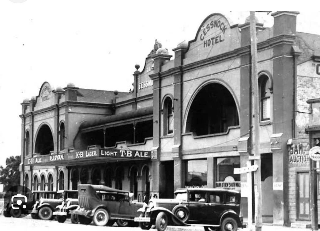 Historic black and white photo of a two-story hotel named 'Cessnock Hotel,' with vintage cars parked in front, and an advertisement banner for beer on the building.