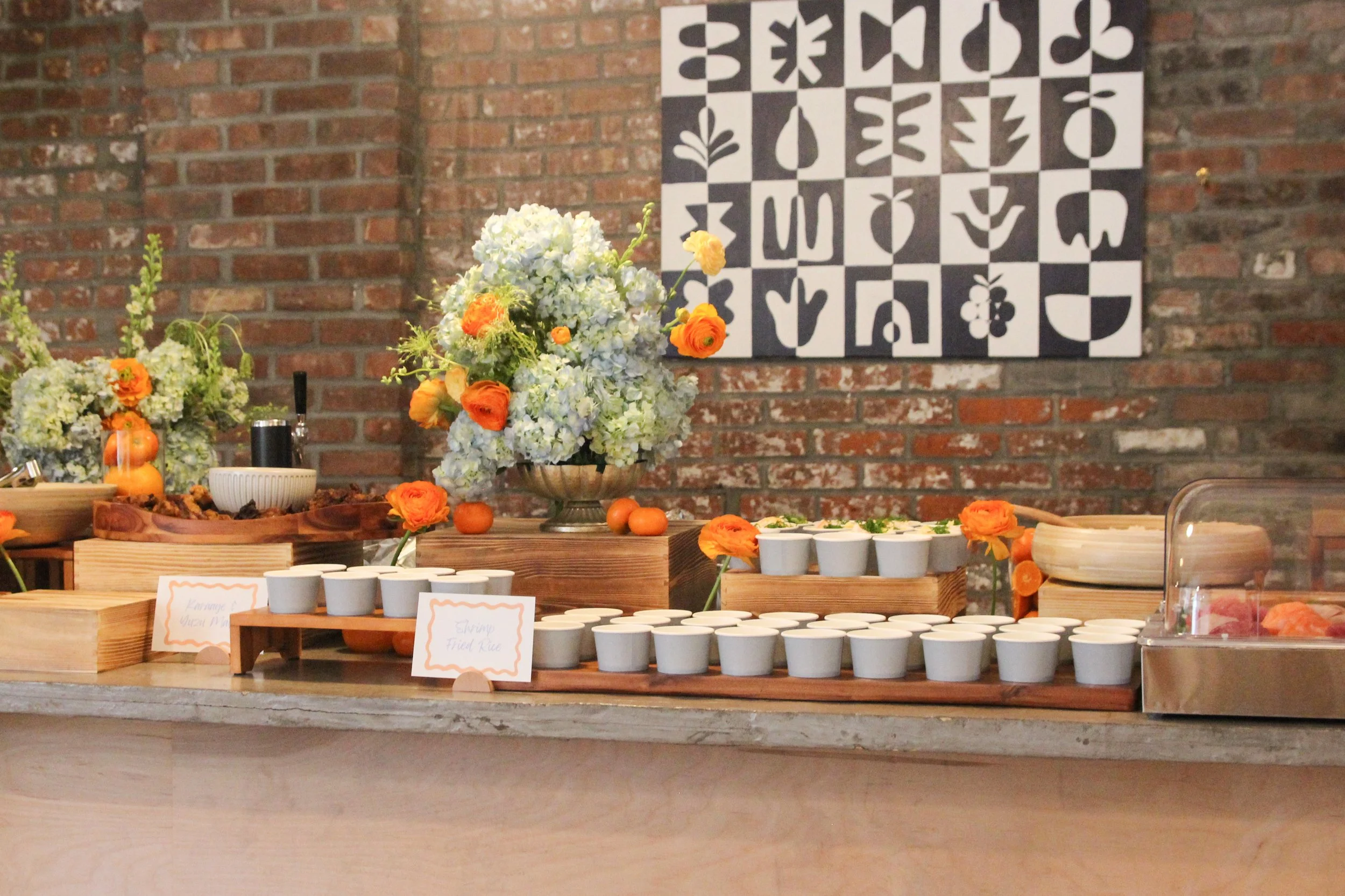 Buffet grazing table with floral arrangements of white and orange flowers.