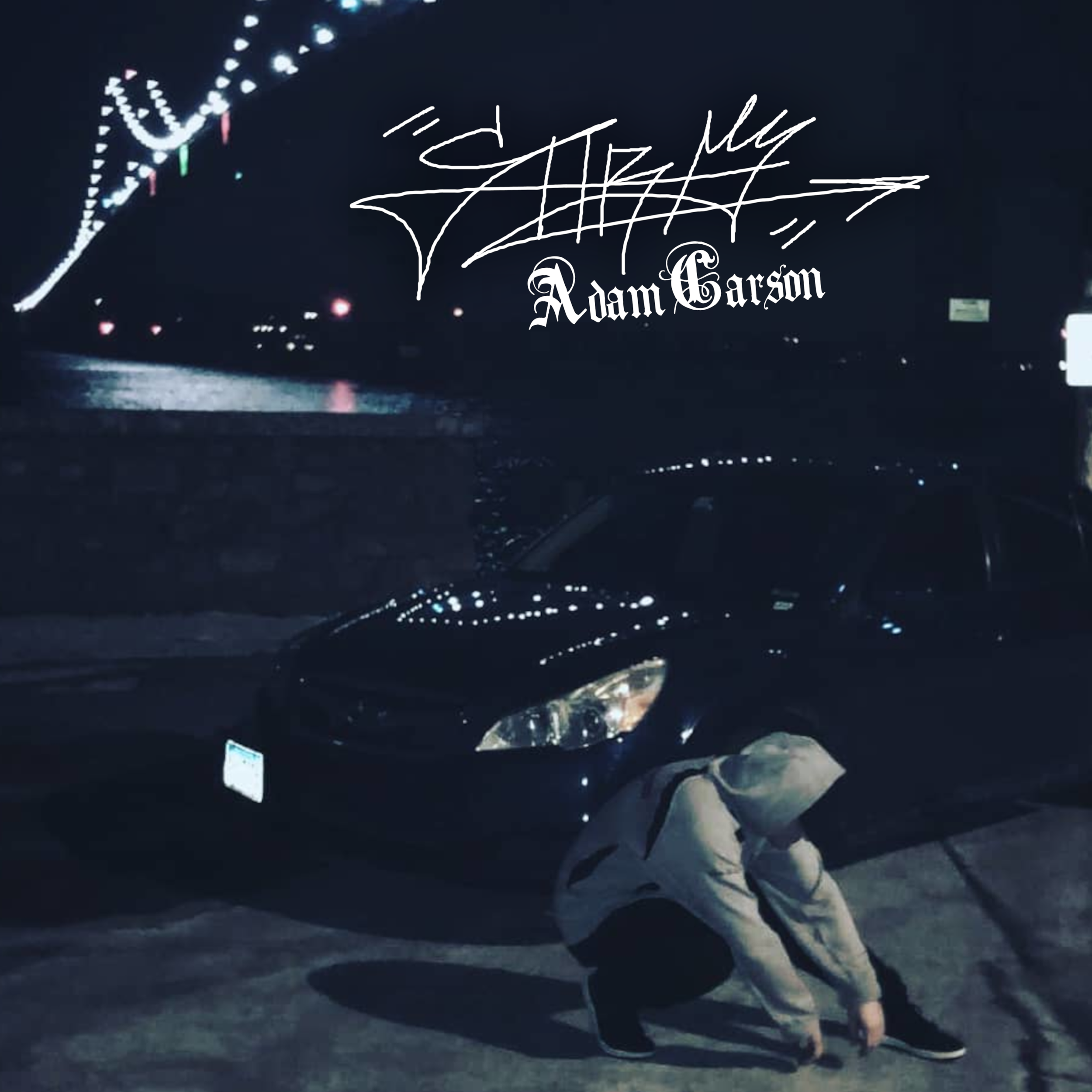 A person is crouching near a black sports car parked on a street at night, with city lights and bridge in the background, and the name 'Adam Garson' along with a signature displayed in the sky.