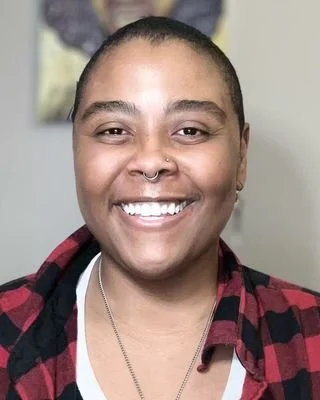 Close-up of a smiling woman with short hair, wearing a plaid shirt and a necklace.