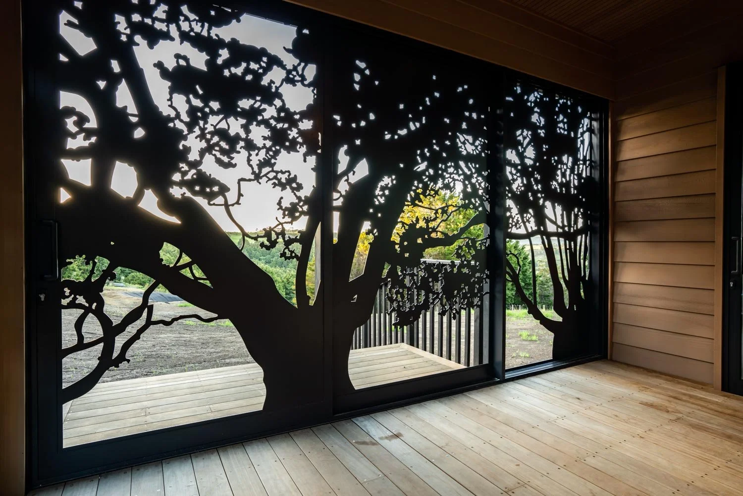 Decorative sliding glass door featuring a silhouette of a tree with intricate branches and leaves, leading to an outdoor landscape with trees and open sky.