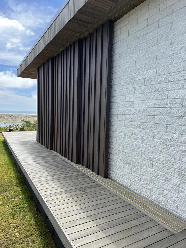 A modern building with a wooden deck, black vertical siding, and a white brick wall. View of a partly cloudy sky and distant landscape.