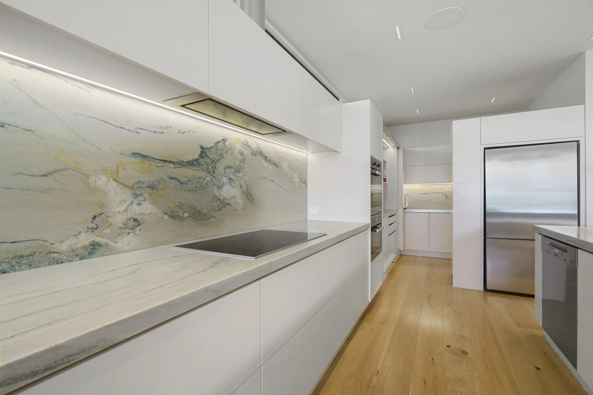 Modern kitchen with white cabinetry, marble backsplash, and wooden flooring.