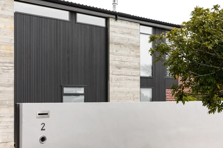 Modern multi-story house with black and light wood exterior, large windows, and a white front wall with the number 2 and a mailbox.
