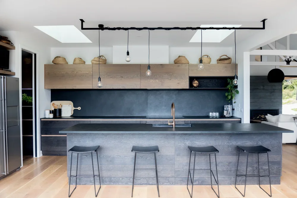 Modern kitchen with gray island, black and wood cabinetry, pendant lights, and stools.