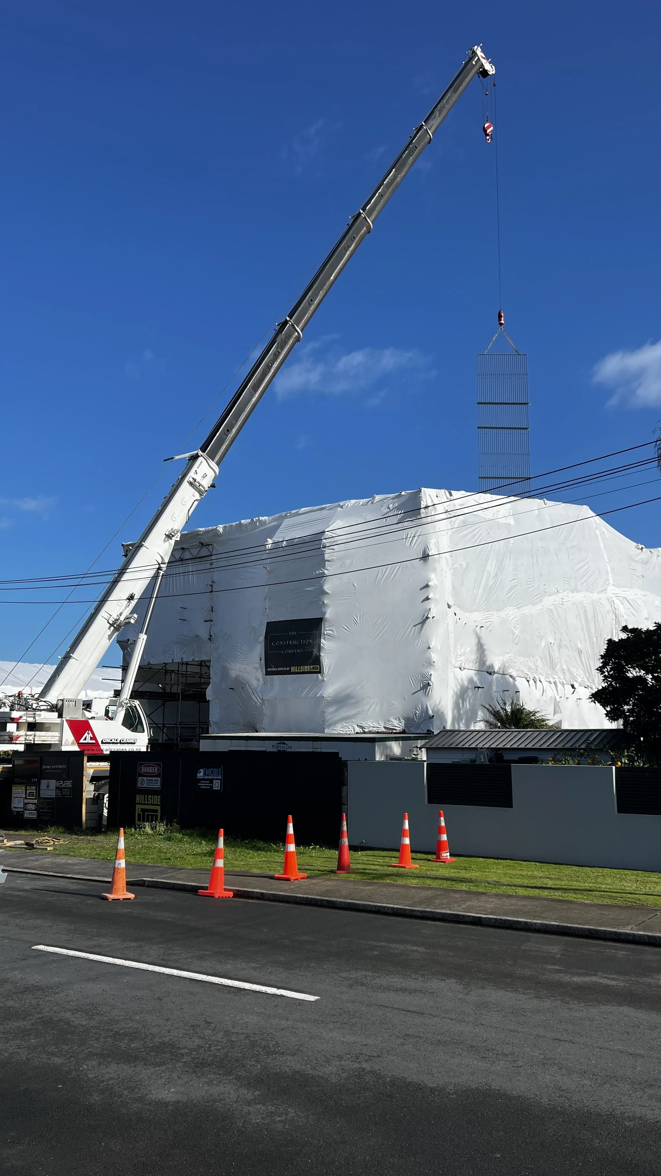 Crane lifting a large 8.5m steel feature stairwell structure on a construction site covered with white protective wrap