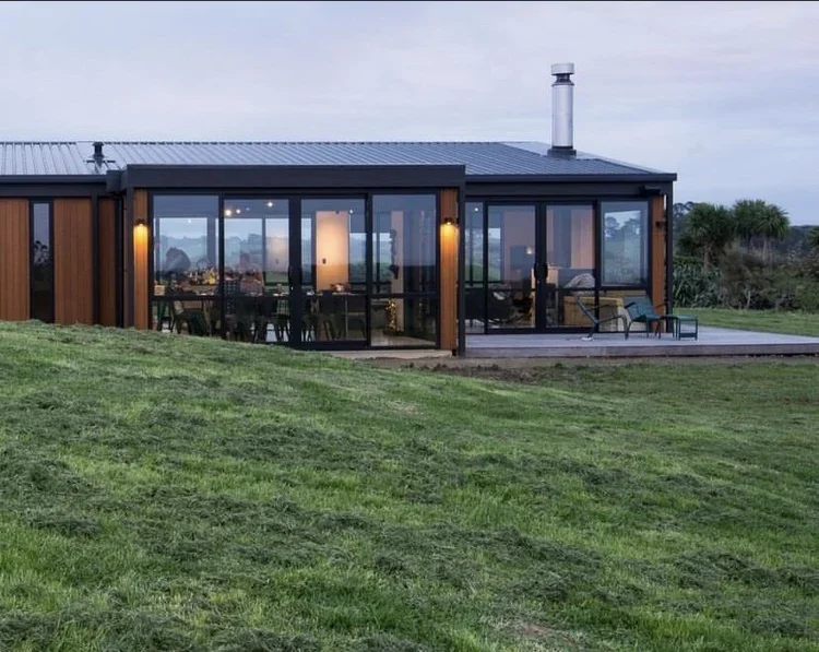 Modern house with large glass windows and a sliding door, situated on a grassy lawn during the day.