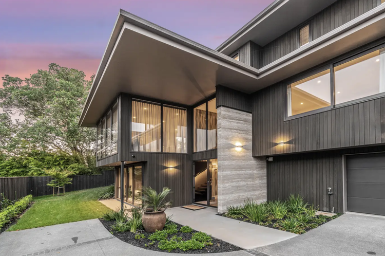 Modern custom-built multi-story house with black cladded exterior, feature travertine tiles, large windows, and landscaped front yard at sunset.