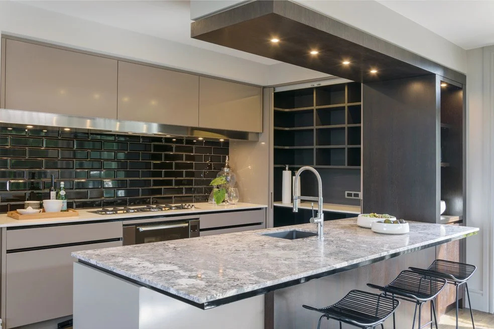 Modern kitchen with black subway tile backsplash, beige cabinets, granite countertop island, black open shelving, and three black bar stools.