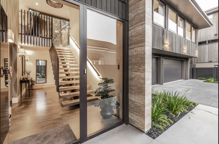 View of modern house entrance with large glass sliding door, wooden staircase, and interior with hardwood floors and minimal decor.