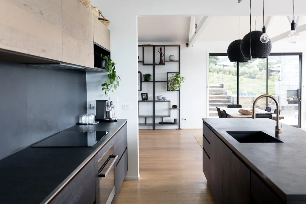Modern kitchen with black countertops, open shelving, and a dining area with black hanging lights and large sliding glass doors.