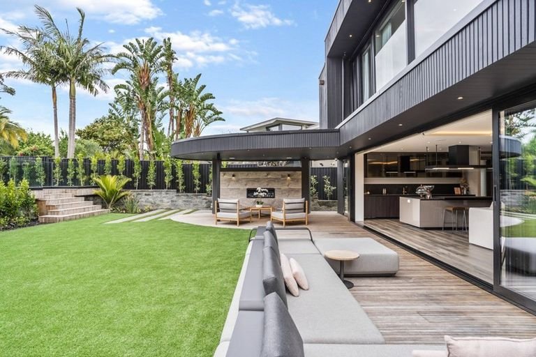 Modern backyard with a well-maintained grass lawn, outdoor seating area, and a covered rounded patio with sliding glass doors leading to an indoor living space. Tall palm trees and lush greenery in the background.
